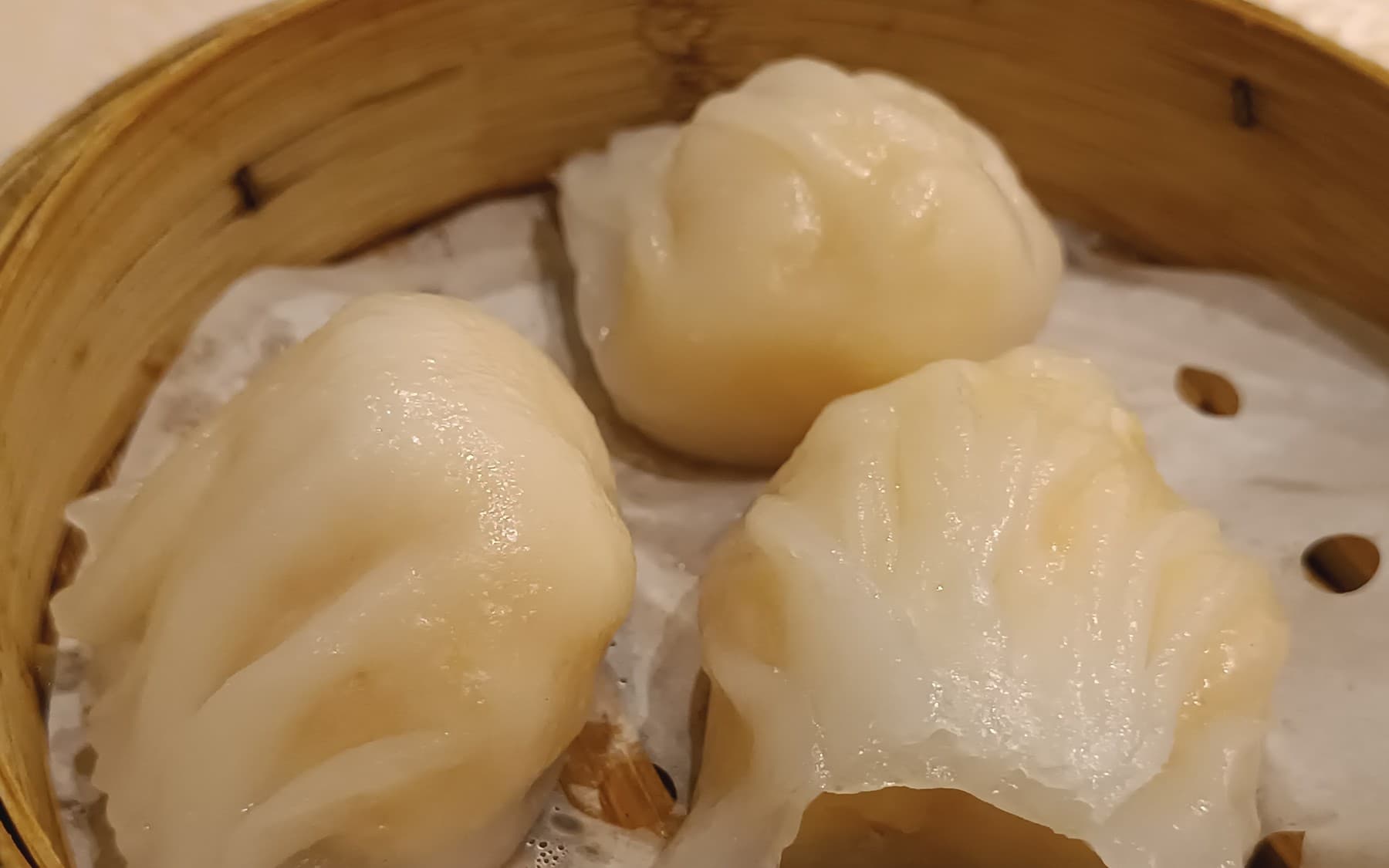 Three shrimp dumplings in a round bamboo steamer