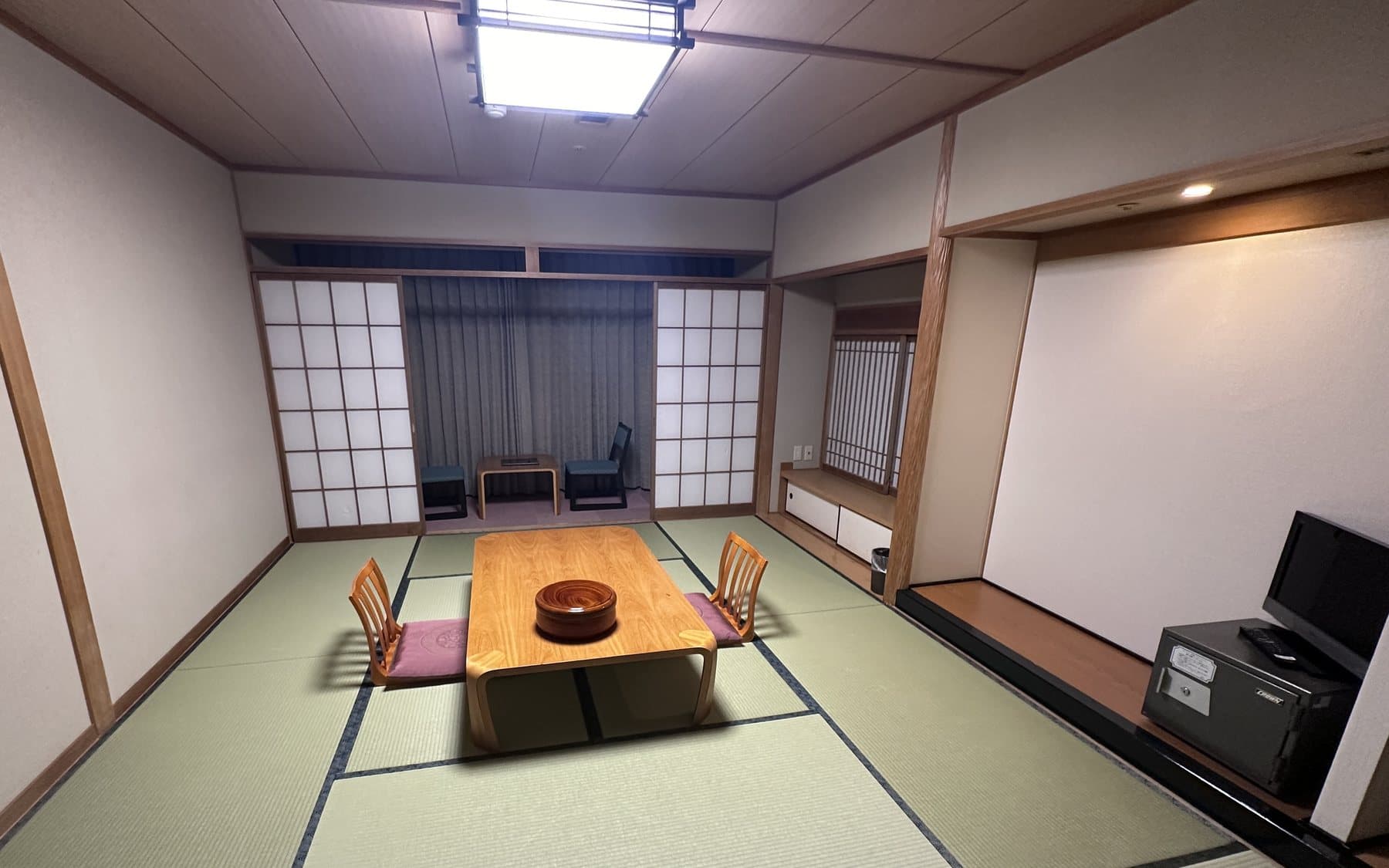 Tatami room in a Japanese inn, with a low wooden table, two chairs, shoji screens, and a television