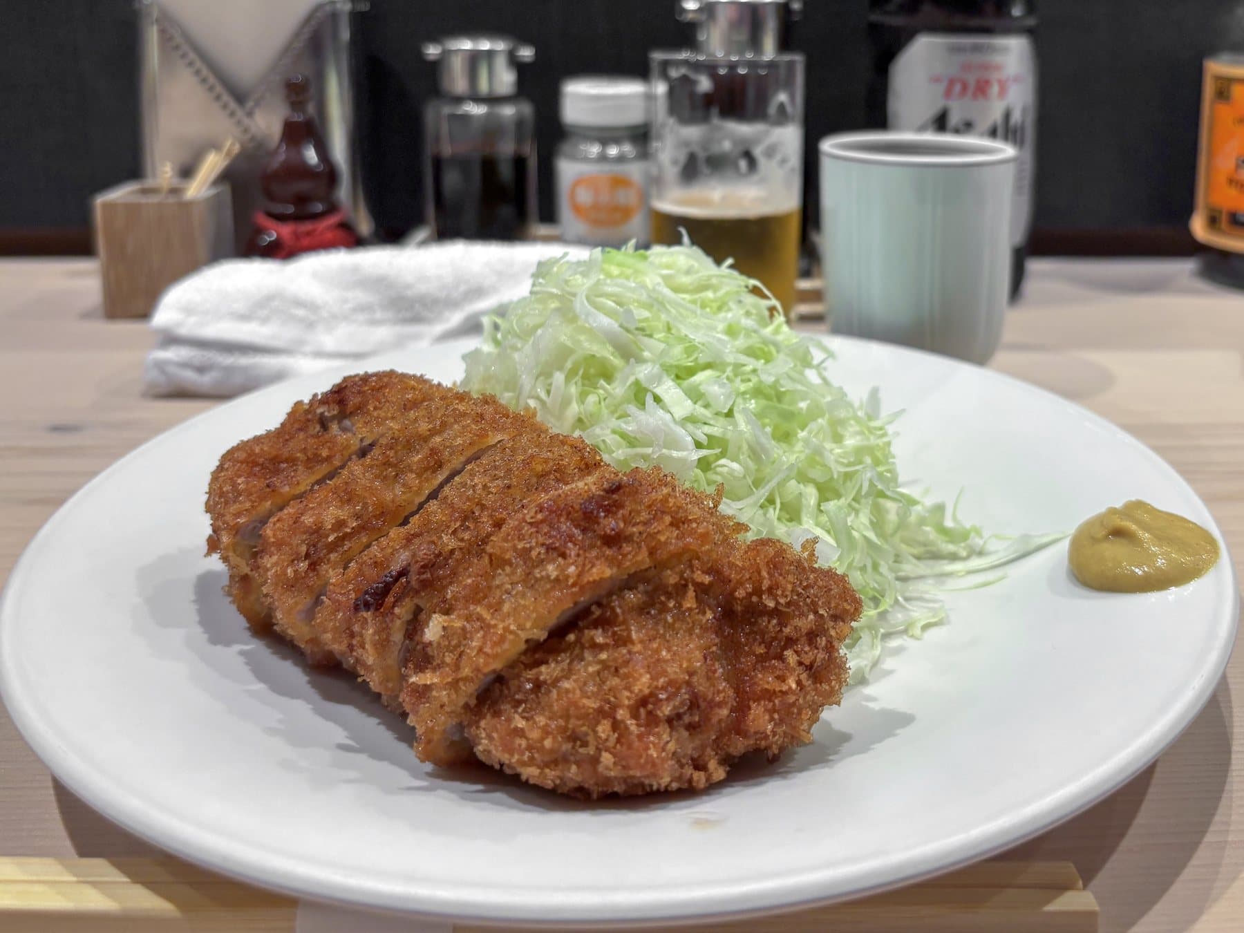 A sliced pork cutlet with shredded cabbage and mustard on a white plate